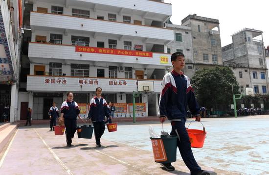 3名學生在廣西橫縣民族中學提著垃圾分類好的垃圾,準備投放到學校準備外運的垃圾桶(4月13日攝)。 新華社記者 周華 攝